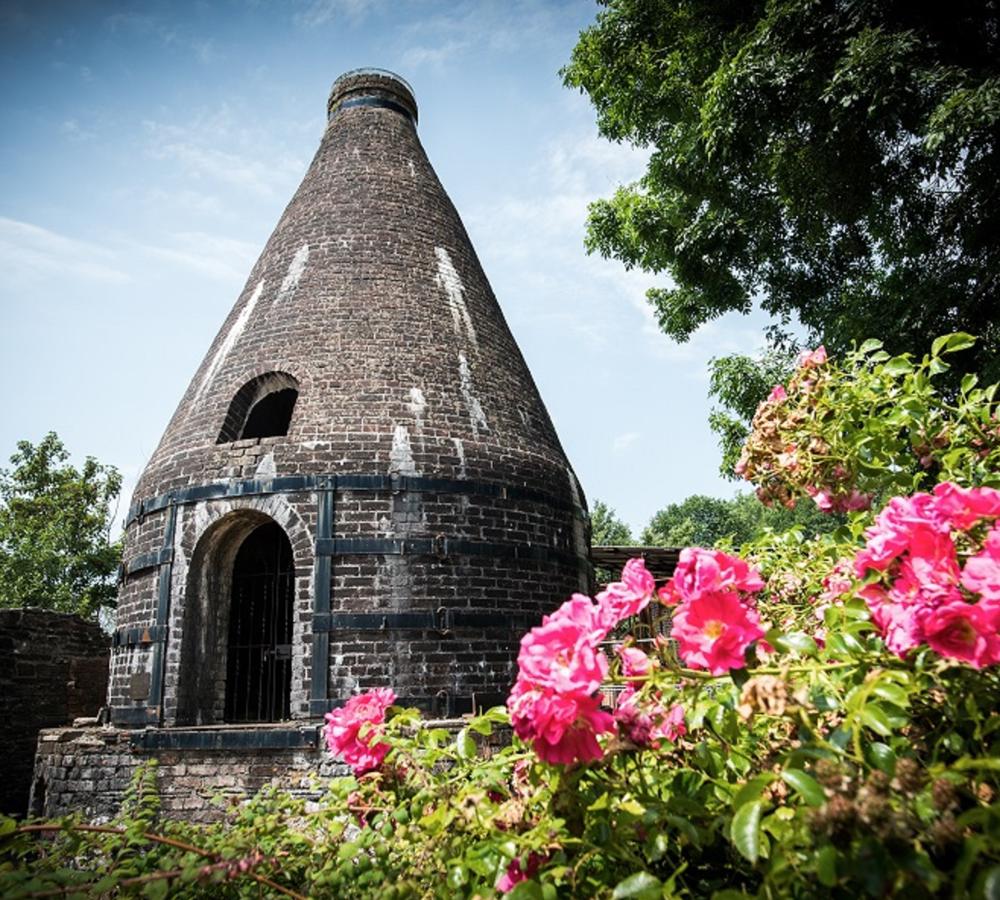 The original conical pottery  kiln at Nantgarw China Works Museum, surrounded by flowers and trees.